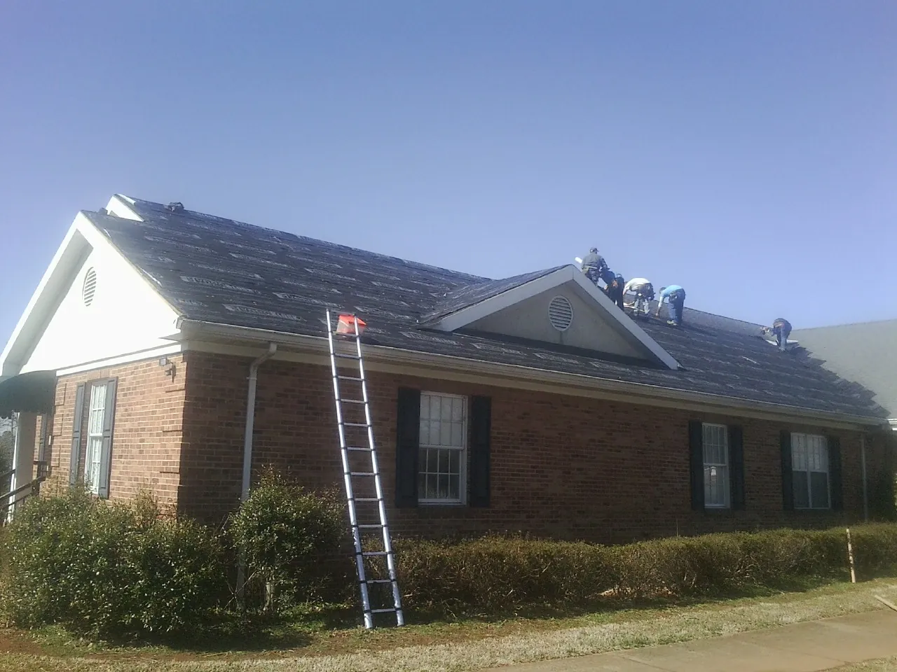 Crew tearing shingles off a brick ranch roof with a ladder set — Metal Roof Repair work by our crew in Ramona