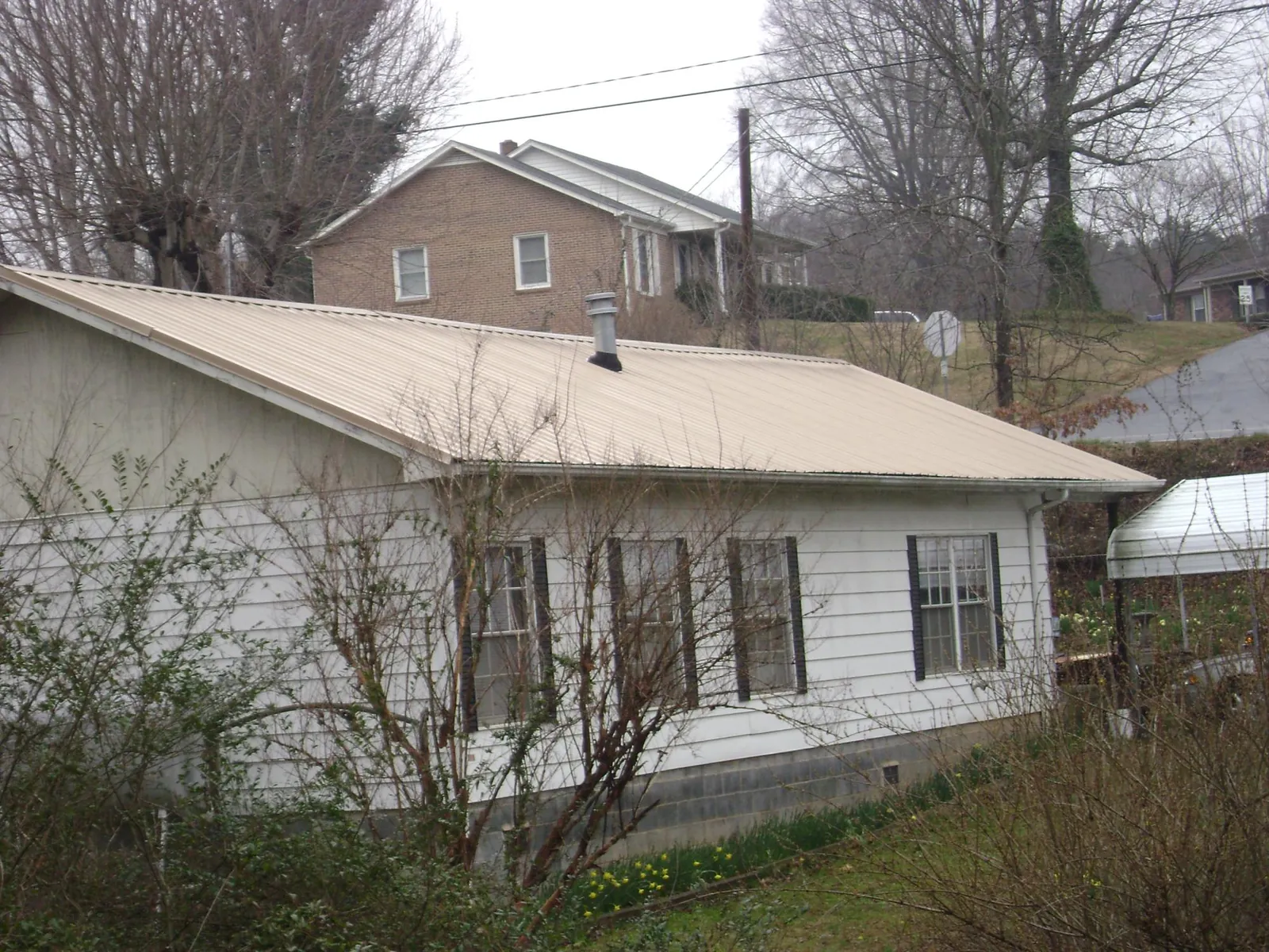 Tan metal roof on a white sided house set into a hillside — Commercial Roofing by Roofing Brothers in Ramona